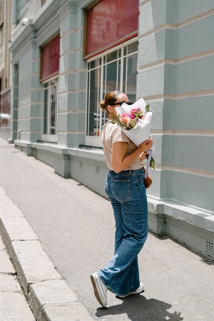 A woman walking on a sidewalk holding a pink bouquet.