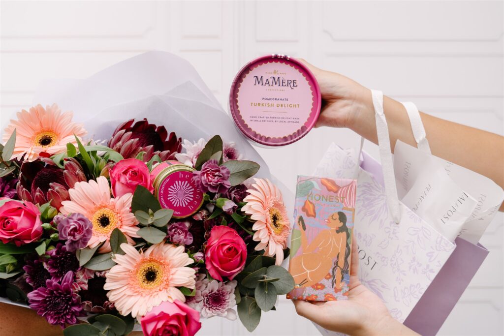 A bouquet of pink and purple flowers with a pink candle, turkish delight, a chocolate and a gift bag.